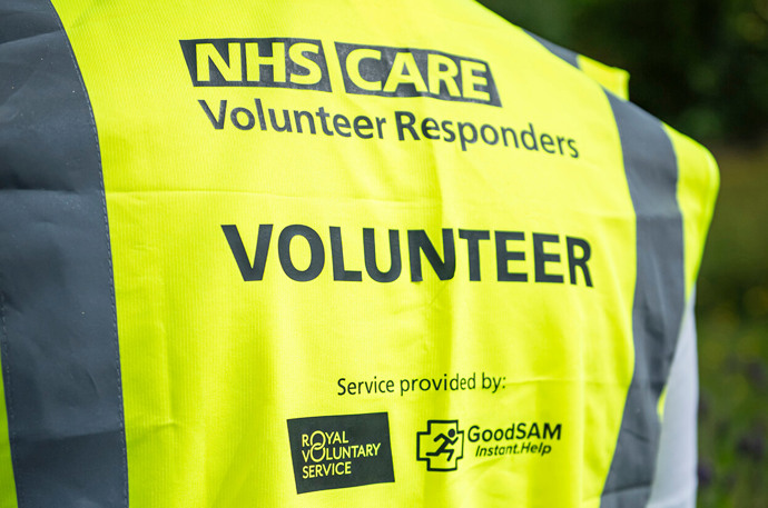 The back of a volunteer wearing a hiviz vest showing NHS and Care Volunteer Responder logo 