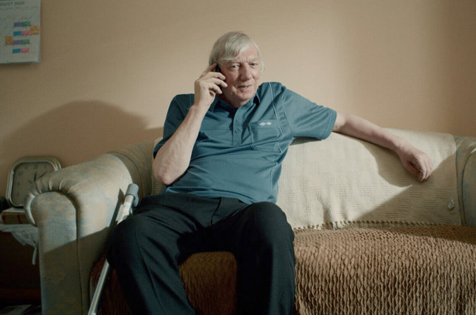 An older man sitting on a sofa on his phone 