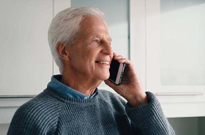 An older man smiling while talking on the phone 