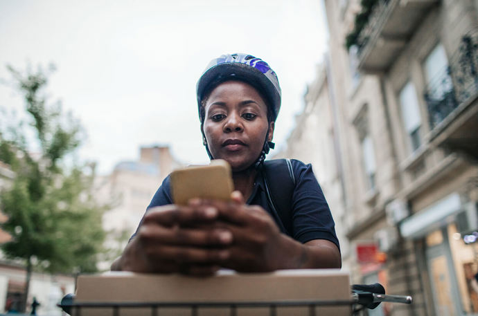 A black delivery cyclist on her phone