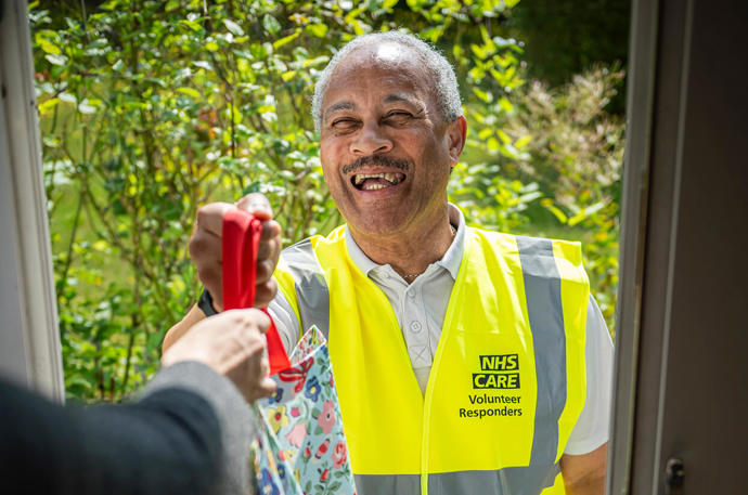 A smiling Community Response Volunteer handing over a bag with shopping 