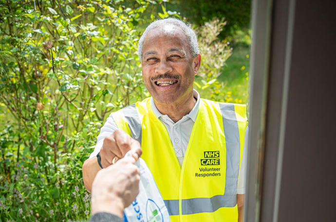 A smiling Volunteer Responder handing over a bacg with a prescription 