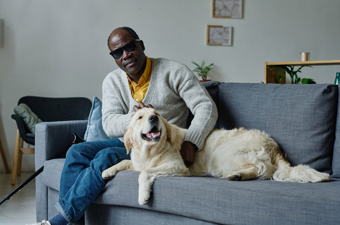 A blind man sitting on a sofa with his guide dog