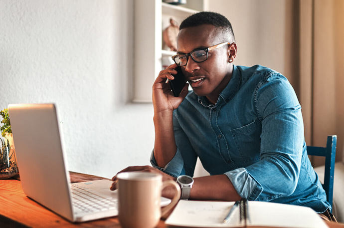 A young man sitting at a computer on his mobile phone