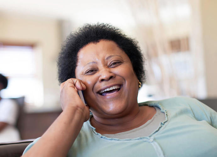 A woman smiling at a camera while speaking on a mobile phone 